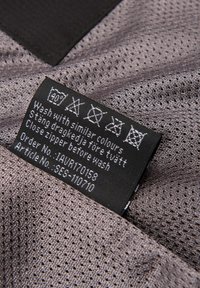 Waslabel op grijze meshstof met was symbolen en instructies om met vergelijkbare kleuren te wassen en de rits te sluiten voor het wassen.