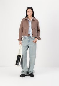 Bruine crop jacket met twee voorzakken, knoopsluiting en een kraag. Gecombineerd met lichtblauwe denim jeans en een harige handtas.