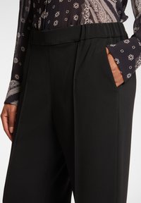 Czarne spodnie z szerokim pasem, bocznymi kieszeniami i gładką, teksturowaną tkaniną, w połączeniu z bluzką z wzorzystymi rękawami.