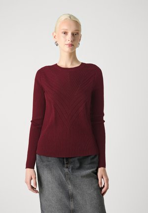 Pull en tricot côtelé bourgogne avec un motif en chevrons, un col rond et des manches longues, associé à une jupe en denim grise.