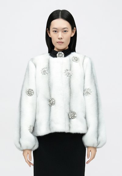 Weiße Pelzjacke mit juwelenartigen Blumenakzenten, lockerem Schnitt, hohem Kragen und voluminösen Ärmeln. Glatte Textur und plüschiges Aussehen.