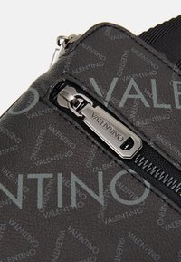 Svart texturerad Valentino-påse med upprepande logotypmönster och en silverfärgad dragkedja med ingraverad "Valentino."