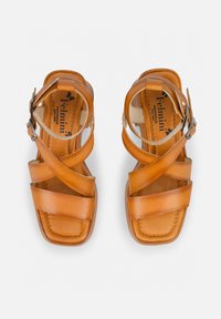 Tan leather sandals featuring crisscross straps, a square toe, and an adjustable ankle buckle. Smooth texture with a cushioned insole.