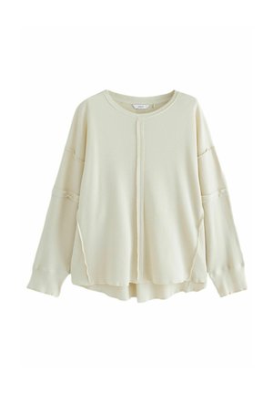 Kremowy sweter z długim rękawem o fakturze gofru, z okrągłym dekoltem, opadającymi ramionami, detalem w postaci środkowego szwu i lekko zaokrąglonym dołem.