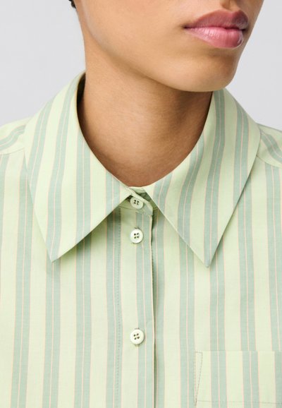 Camicia con colletto in cotone verde chiaro con righe verticali di un verde più scuro e pesco. Presenta due bottoni e una tasca sul petto.