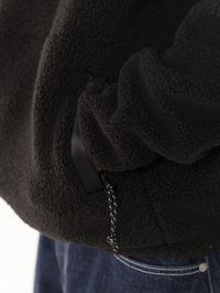 Giacca in pile nera con una superficie testurizzata, tasca laterale con bordo in tessuto nero e coulisse regolabile con motivo in contrasto.