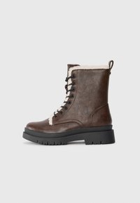 Brune lærsnøresko med faux pelskant, sort gummisål og runde snørebånd. Har en løftetabel på hælen for nem påtagning.