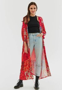 Plyšový červený kimono s živými vzory paisley; lehký materiál, dlouhé rukávy, otevřený střih, spárováno s černým tílkem a džíny.