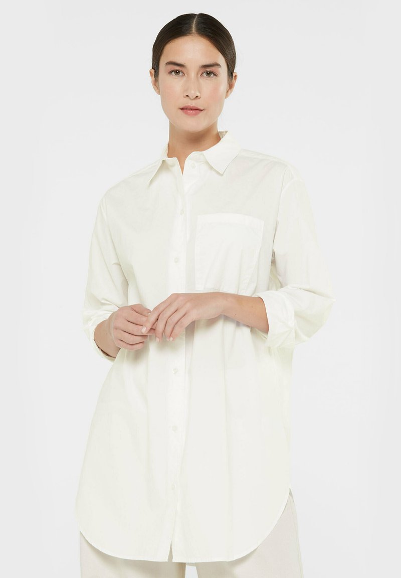 White, long-sleeve button-up shirt made of lightweight fabric, featuring a collar and a chest pocket, with a curved hem and relaxed fit.