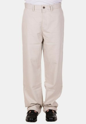 Pantaloni beige a gamba dritta indossati con mocassini intrecciati in pelle nera, mostrati dalla vita ai piedi su uno sfondo semplice.