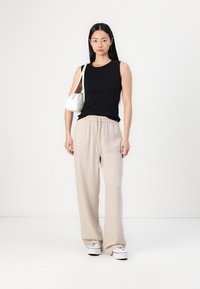 Black sleeveless top, beige wide-leg pants, white sneakers, and small white handbag. Simple design with a relaxed fit and textured fabric.