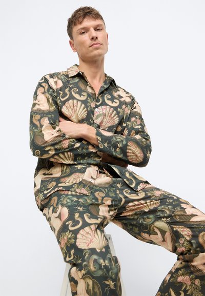 Set de loungewear cu un model prezentând un fundal verde închis cu motive clasice roz și bej, inclusiv scoici și figuri. Material moale.