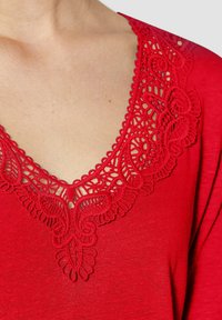 Rode kleding met ingewikkelde kantdetails rond de halslijn. Het materiaal lijkt zacht met een gladde textuur. Heeft een V-vormige kraag.