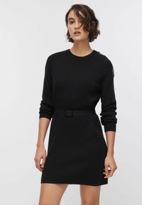 Robe noire en maille avec un col rond, des manches longues et une taille ceinturée. Comprend des poignets côtelés et des détails décoratifs aux épaules.