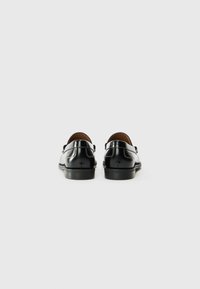 Schwarze Lederschuhe mit glatter Oberfläche, abgerundeten Fersen und einem kontrastierenden hellen Stich entlang der Ferse. Gummisohlen sichtbar.