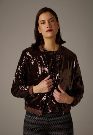 Brown sequined bomber jacket with a ribbed collar and cuffs, zip closure, and a slightly cropped fit, worn over a patterned top.