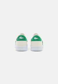 Valged nahast tossud roheliste sametist kandadega ja valgete kummist taldadega, millel on igal kandil väike Lacoste logo.