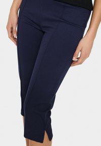 Navy blue cropped pants made of stretchy fabric, featuring side slits at the hem and a smooth texture. No visible hardware or patterns.