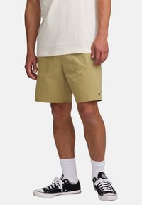 Knee-length, light olive cargo shorts made of lightweight fabric, featuring two front pockets and a small brand label at the hem.