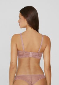 Krajkový bralette v jemné mauve barvě s nastavitelnými ramínky, květinovým vzorem a zapínáním na háček a oko. Viditelný je také odpovídající krajkový thong.