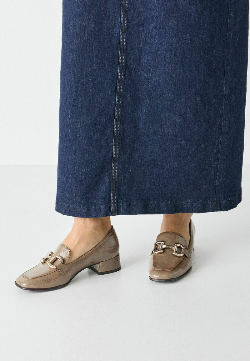 Bruna lackläders loafers med låg klack och dekorativt guldhardware. Bärs med en lång mörk denimkjol.