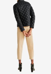 Veste matelassée noire avec un col montant, associée à un pantalon beige cropped et des bottines noires, vue de dos.