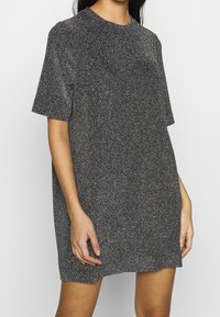 Vestido corto negro de corte suelto, con mangas cortas, hecho de una tela texturizada con efecto brillante, que presenta un escote redondo.