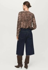 Blusa a stampa leopardata marrone, culotte in denim scuro e stivali al ginocchio marroni. La blusa presenta una vestibilità comoda e arricciature al collo.