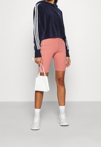 Mörkblå velourcroppad hoodie med vita ränder, kombinerad med ljusrosa cykelshorts. Accessoarer inkluderar en liten vit texturerad handväska och vita sneakers.