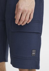 Shorts cargo bleu marine en tissu doux, dotés de poches latérales, de coutures texturées et d'un petit patch noir avec un texte blanc.