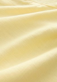 Svetložltá tkanina s mäkkým, textúrovaným vzorom; hladký povrch s jemnými líniami a ľahkým vzhľadom, ideálna pre rôzne textilné použitia.