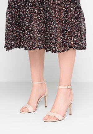 Beżowe sandały na wysokim obcasie z paskiem wokół kostki, charakteryzujące się gładkim wykończeniem ze skóry i kwadratowym noskiem, umieszczone na neutralnym tle.