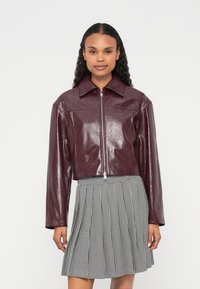 Vinrde lažni usnjeni kratki suknjič z zareznim ovratnikom in zadrgo spredaj, kombiniran s črno-belim karo plise krilom.