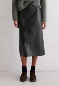 Czarna skórzana spódnica midi o gładkiej fakturze, z detalami szwów i prostym krojem. W zestawie z brązowymi butami i czarnymi skarpetkami.