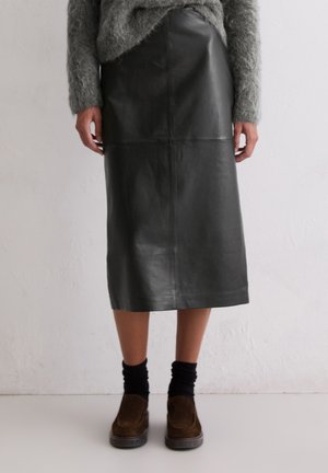 Zwarte leren midi-rok met een gladde textuur, voorzien van naaddetails en een rechte snit. Gecombineerd met bruine schoenen en zwarte sokken.