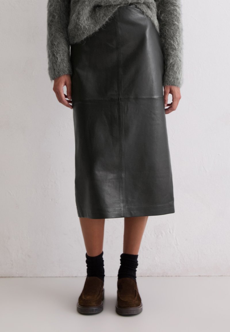 Czarna skórzana spódnica midi o gładkiej fakturze, z detalami szwów i prostym krojem. W zestawie z brązowymi butami i czarnymi skarpetkami.