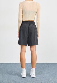 Beige ribbad långärmad topp och svarta cargoshorts med elastisk midja. Vita sneakers och strumpor i mellanhöjd fulländar outfiten.