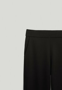 Pantalons noirs taille haute avec poches latérales et large ceinture, présentés sur un fond clair uni.