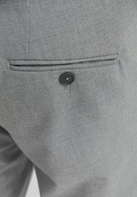 Pilkos tekstūros audinys iš kostiumo kišenės su maža juoda užsegimu. Kišenė turi modernų dizainą su įpjova.