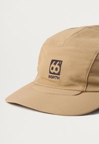 Gorra caqui hecha de tela suave, con visera curva, detalles de costura vertical y un logo bordado oscuro "66° North" en la parte frontal.