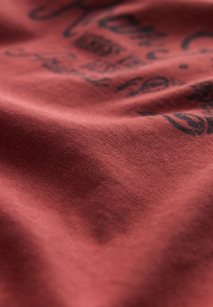 Roter Baumwollstoff mit weicher Textur, der ein schwarzes, bedrucktes Design mit komplizierten Mustern und Schriftzügen zeigt.