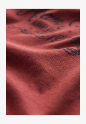 Czerwona bawełniana tkanina o miękkiej fakturze, z czarnym nadrukiem zawierającym misternie wykonane wzory i napisy.