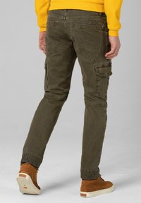 Khaki Cargo-Hosen mit mehreren Taschen, schmal zulaufenden Beinen und elastischen Bündchen, kombiniert mit braunen High-Top-Schuhen. Glattes Baumwollgewebe.