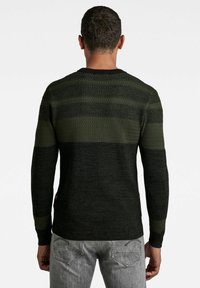 Ciemnozielony sweter z teksturowanymi paskami w różnych odcieniach, z prążkowanym okrągłym dekoltem i dopasowanymi rękawami, w zestawie z szarymi dżinsami.