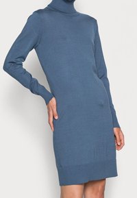 Robe en tricot bleu avec un col montant, des manches longues, des poignets et un ourlet côtelés. Texture lisse, design ajusté et légère extensibilité pour le confort.