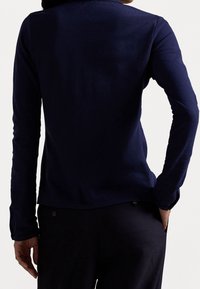 Námořnická modrá dlouhá rukávová halenka s kulatým výstřihem, vyrobená z hladkého materiálu. Zadní strana se vyznačuje jednoduchým, čistým designem bez viditelných švů nebo log.