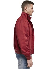 Veste bomber rouge avec un col montant, en tissu lisse, dotée d'une fermeture éclair à l'avant, de poignets côtelés et de poches latérales.