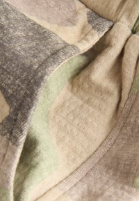 Tissu tricoté doux avec des blocs de couleur beige, gris et vert clair, montrant la texture détaillée et les coutures en gros plan.