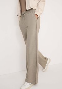 Pantalons de survêtement larges, gris clair, avec une taille élastique et un cordon de serrage, dotés de poches latérales et d'une texture de tissu lisse.