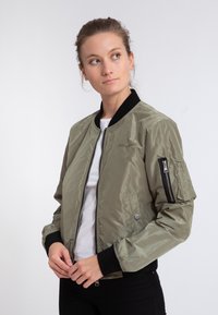 Olivegrüne Bomberjacke aus glänzendem Nylon, mit Reißverschluss vorne, gerippten Bündchen und einer Reißverschlusstasche an einem Ärmel. Dezent ausführliches Logo auf der Brust.